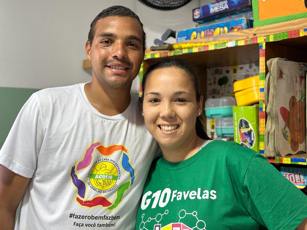 Na imagem, temos Mateus (à esquerda) e Tifanny (à direita). Mateus veste uma camiseta branca com um símbolo colorido com os dizeres "#fazerobemfazbem, faça você também". Tifanny veste uma camiseta verde com os dizeres "610 favelas". Ambos sorriem para a câmera.